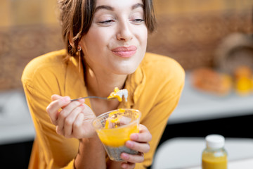 Portrait of a young and cheerful woman eating chia pudding, having a snack or breakfast in the...