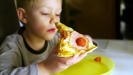 Dziecko zjada kawałek pizzy. Chłopiec trzyma pizzę i patrzy na nią, jest głodny i zjada...