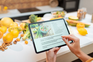 Woman looking on the digital recipe, using touchscreen tablet while cooking healthy meal on the...