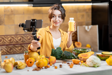 Young and cheerful woman vlogging on mobile phone about healthy food and cooking. Concept of healthy eating and social media influencing