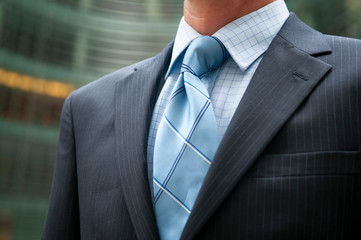 Close-up of unrecognizable businessman in dark pinstripe suit and blue tie standing outdoors in an...