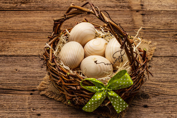 Fototapeta na wymiar Easter wicker basket. Zero waste, DIY concept. Wooden eggs, shavings, satin bow. Old boards background