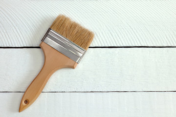 a wide repair paint brush stands on white painted boards, do-it-yourself repair concept