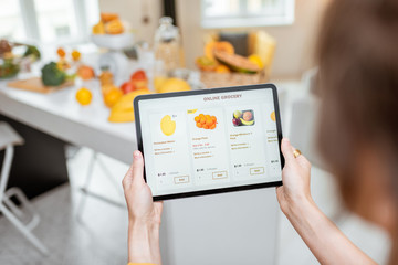 Woman shopping food online using a digital tablet at the kitchen, close-up view on a tablet screen. Concept of buying online using mobile devices
