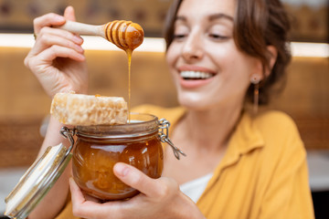 Portrait of a young and cheerful woman with a jar full of sweet honey on the kitchen at home