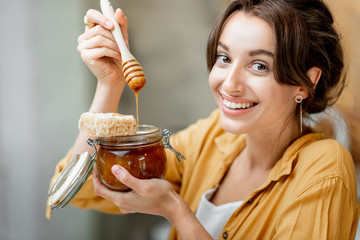 Portrait of a young and cheerful woman with a jar full of sweet honey on the kitchen at home