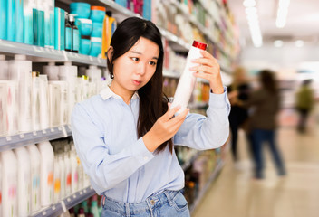Portrait of young Asian woman choosing shampoo in supermarket