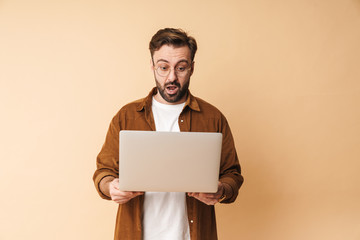 Shocked young unshaved man using laptop computer.