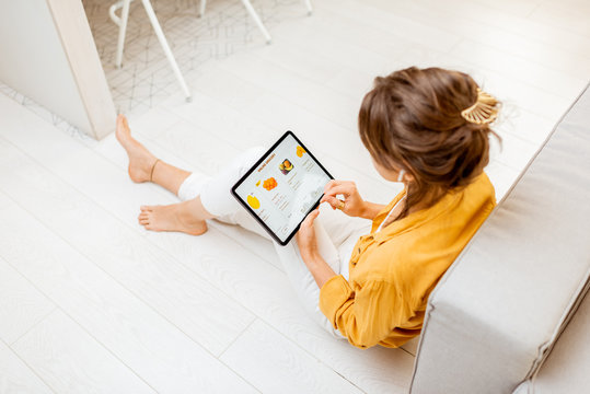 Young woman shopping fresh food online using a digital tablet, while sitting on the floor at home. Concept of buying online using mobile devices