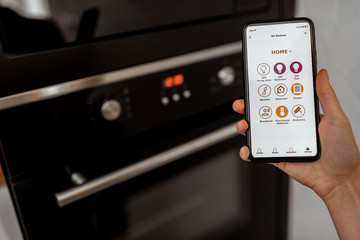 Controlling smart kitchen appliance using mobile phone at home, close-up on mobile screen. Concept of a smart home and managing home with mobile devices