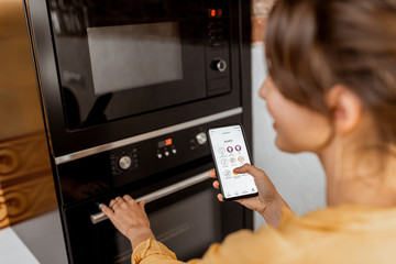 Woman controlling smart kitchen appliance using mobile phone at home, close-up on mobile screen....