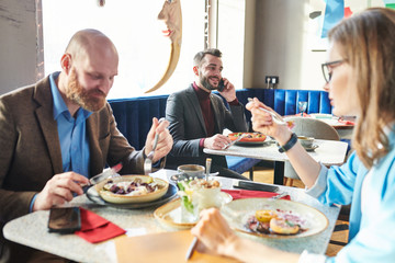 Business people in cafe: successful young businessman eating salad and discussing business on phone...