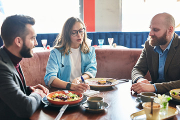 Enterprising businesswoman in glasses making notes while offering strategy for new project to colleagues