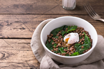 Boiled lentils with spinach, herbs, spices and poached egg in ceramic bowls on wooden background. Simple healthy homemade food	