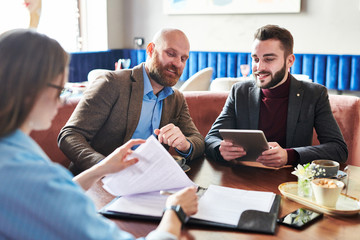 Businessmen answering questions on contract to lady while she signing contract in cafe