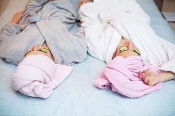 Two girlfriends with towels on their heads, doing spa treatments at home in bed