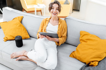 Young and cheerful woman using a digital tablet while sitting relaxed on the couch at home. Concept of a leisure activities with mobile devices at home © rh2010