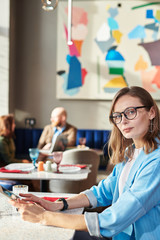 Portrait of serious beautiful middle-aged businesswoman in glasses checking email on tablet in restaurant