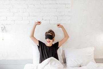 Fototapeta na wymiar Young woman in sleeping mask waking up in the bedroom. Good morning concept