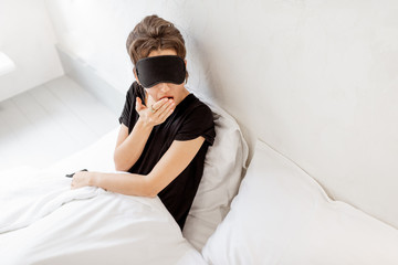 Portrait of a young woman in sleeping mask sitting in bed during a morning time