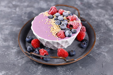 Fruit smoothie bowl with pink yogurt decorated with healthy raspberry, blueberry and puffed quinoa grain on iron tray 