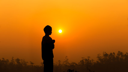 Fototapeta premium Human standing and praying with light sunset background, christian silhouette concept.
