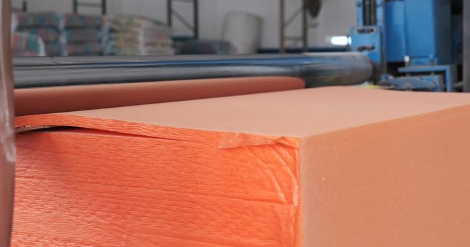 Modern factory for working with foam rubber. At initial stage of production, orange cube passes through knife; produces blanks for household, industrial goods. sponges are presented in various colors