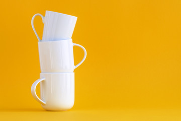 Three white coffee cups stacked on yellow background