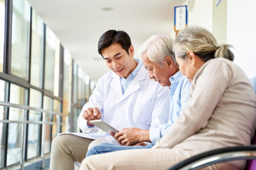 young asian doctor talking to senior couple patients in hospital hallway