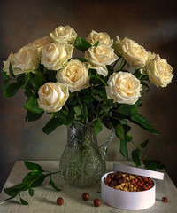 A beautiful bouquet of roses in a crystal jug and a box with tasty nuts. Still life. Vintage.