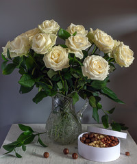 A beautiful bouquet of roses in a crystal jug and a box with tasty nuts. Still life. Vintage.