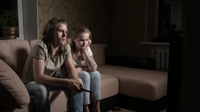 Young couple is watching tv. Man switches channels, woman selects control.