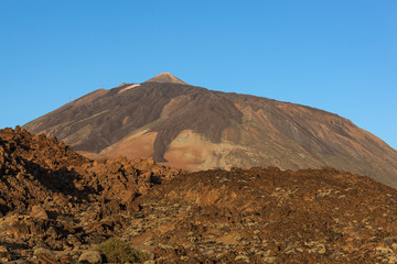 Majestic red volcanic terrain in the Teide national park with Teide Mount on the blue sky background in Tenerife, Canary Islands, Spain