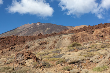 Fototapeta na wymiar Majestic red volcanic terrain in the Teide national park with Teide Mount on the blue sky background in Tenerife, Canary Islands, Spain