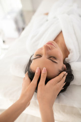 Dark-haired woman lin a white robe having face massage