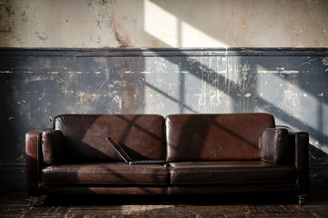 brown leather sofa against an old gray wall with cracked paint in the sun, a room with furniture