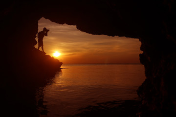Silhouette of photographer using the camera to take photo of the sunset in a cave by the sea