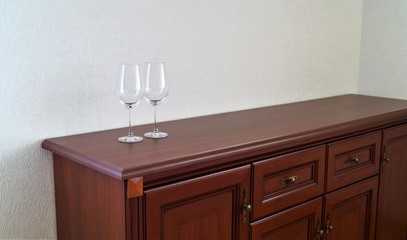 two wine glasses on a wooden chest of drawers on a white wall background
