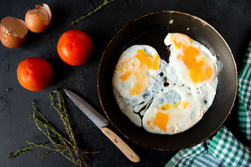 eggs in a frying pan , tomatoes, towel, knife, thyme, shell on a black background