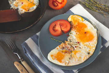 eggs with tomato on a plate on a towel, knife and fork on a gray background