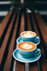 Two cups of cappuccino with latte art on wooden background. Beautiful foam, blue ceramic cups, diagonal composition, place for text.