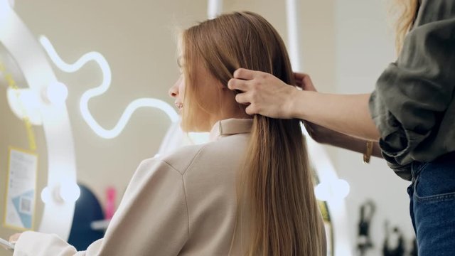 A bottom view of a professional hairdresser is touching long blonde hair of her client at a beauty salon