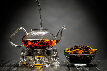 Horizontal photo of the tea set on a black background. Glass transparent teapot and cup. Black leaf...