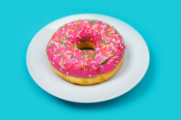 Colorful holey donut cake with pink glaze on white plate and turquoise blue background. Isolated image.