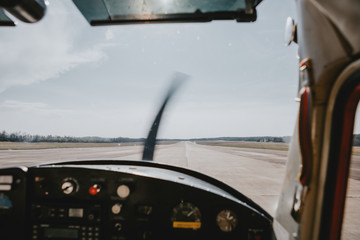 The view from the cockpit of a waiting airplane before take-off on the runway with dashboard and rotating propeller in front and horizon with clear sky in background