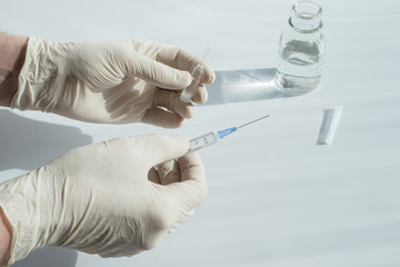 Hands in rubber gloves hold a syringe with a needle and an ampoule with powder for the preparation of an injection. The concept of treatment and prevention of diseases.