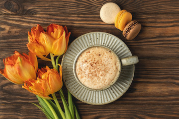 orange tulips, cup with coffee and macaroon cookies on a wooden background, copy space