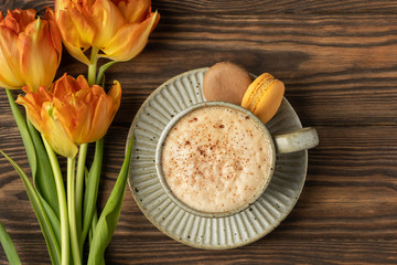 Obraz na płótnie Canvas orange tulips, cup with coffee and macaroon cookies on a wooden background, copy space