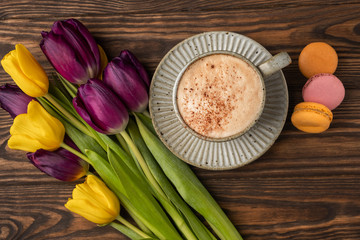 Obraz na płótnie Canvas purple and yellow tulips, cup with coffee and macaroon cookies on a wooden background, copy space