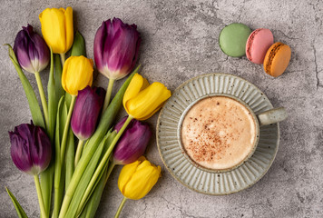 purple and yellow tulips, cup with coffee and macaroon cookies on a gray concrete background, copy space